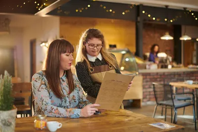 A café server presenting a menu to a smiling customer at a wooden table